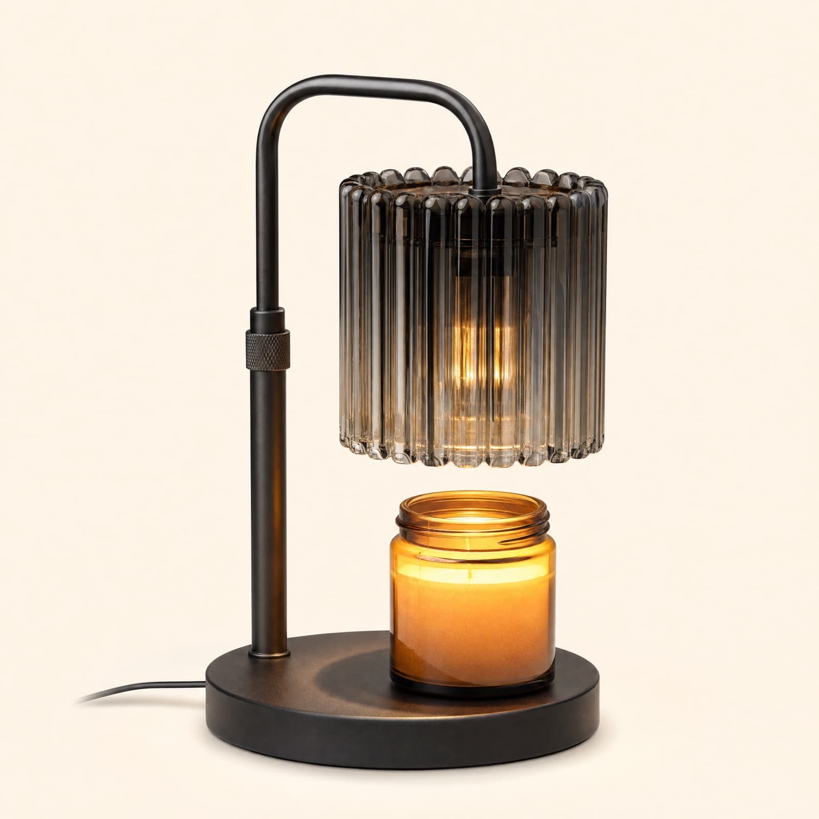 The warmer lamp in Ember Black with bronze hardware, the ribbed glass shade hanging over an amber jar candle with open air between them.